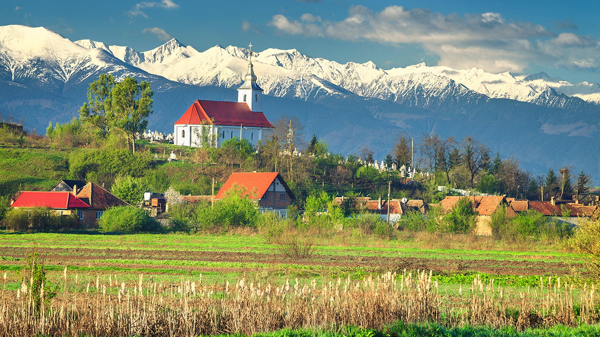 Amazing spring countryside landscape with church of Mandra and high snowy Fagaras mountains in background, Brasov region, Transylvania, Romania, Europe